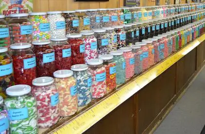 Jars filled with colorful candies lined up on a wooden shelf.